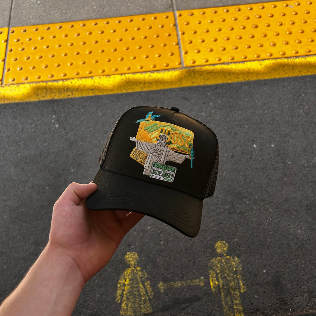 Hand holding a black hat with a yellow and green Brazil themed hat on a yellow tactile paving strip.