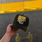 Hand holding a black hat with a yellow and green Brazil themed hat on a yellow tactile paving strip.