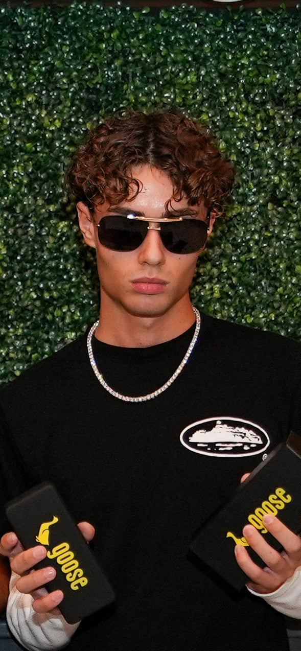 Person holding black phone cases with 'GOOSE' branding against a green leafy background