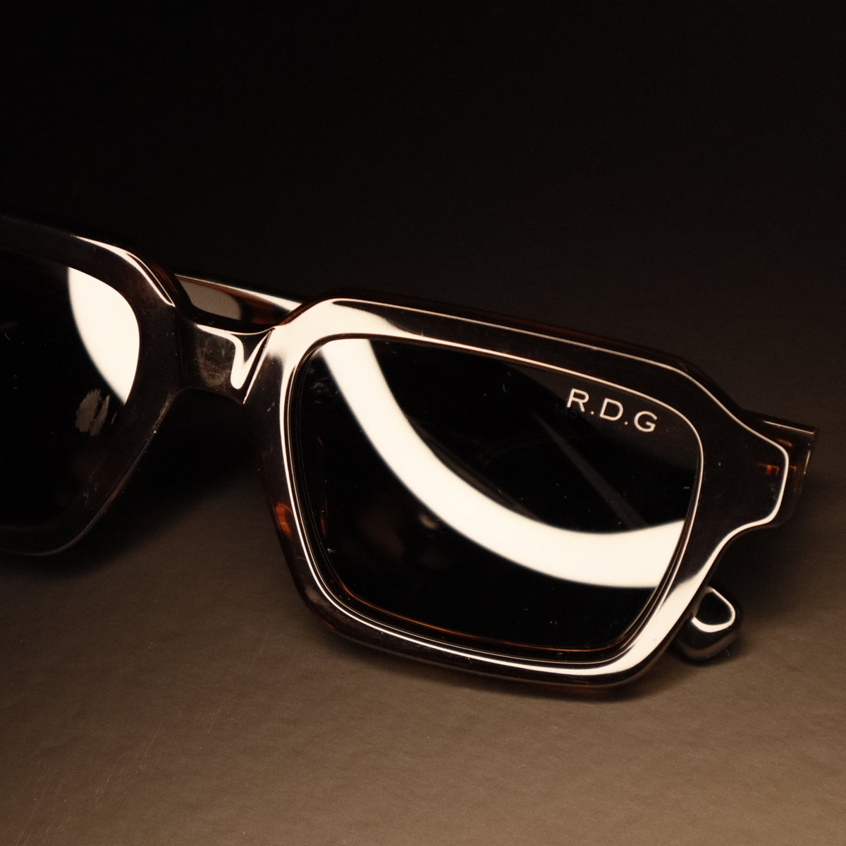 A pair of oversized square sunglasses with a glossy black acetate frame and dark lenses, featuring the brand name 'R.D.
