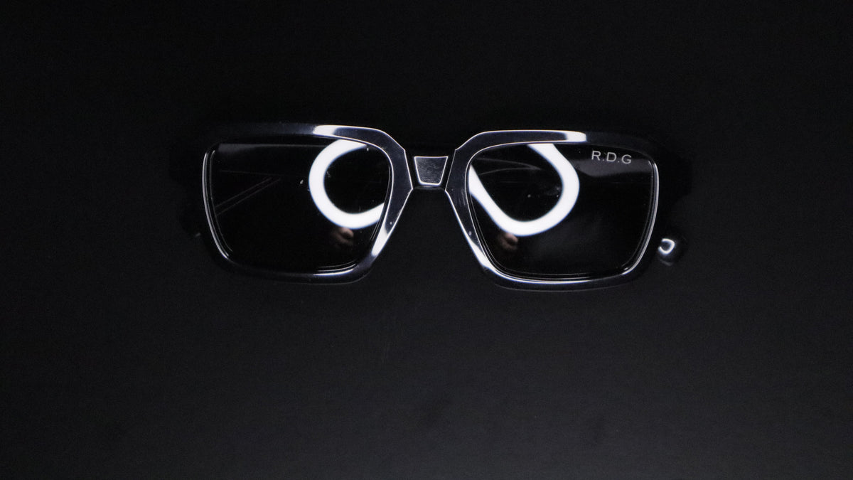 A pair of black framed sunglasses with dark lenses, featuring a small silver 'R.D.G'