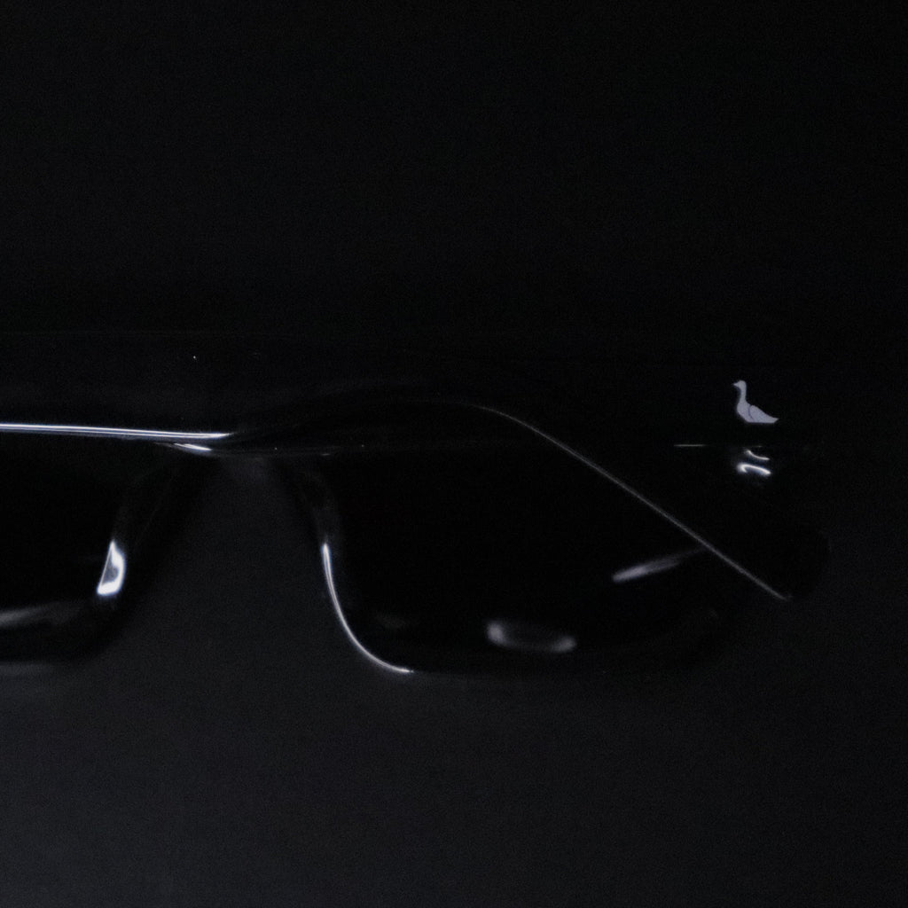 Black square sunglasses with a glossy finish and thin silver metal temples, shown on a solid black background.