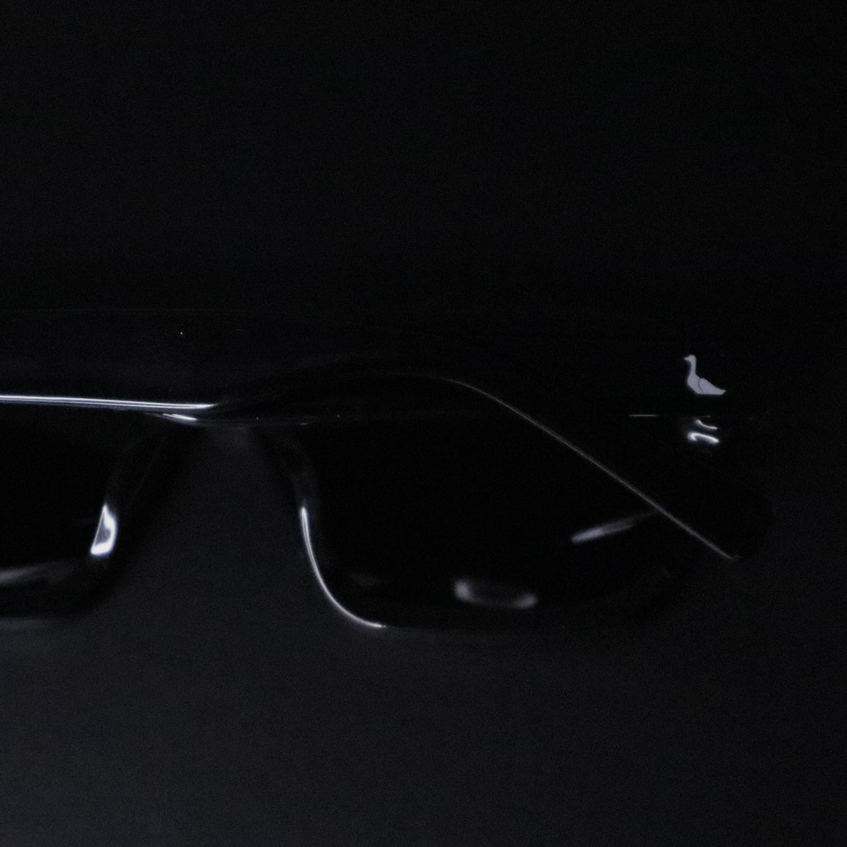 Black square sunglasses with a glossy finish and thin silver metal temples, shown on a solid black background.