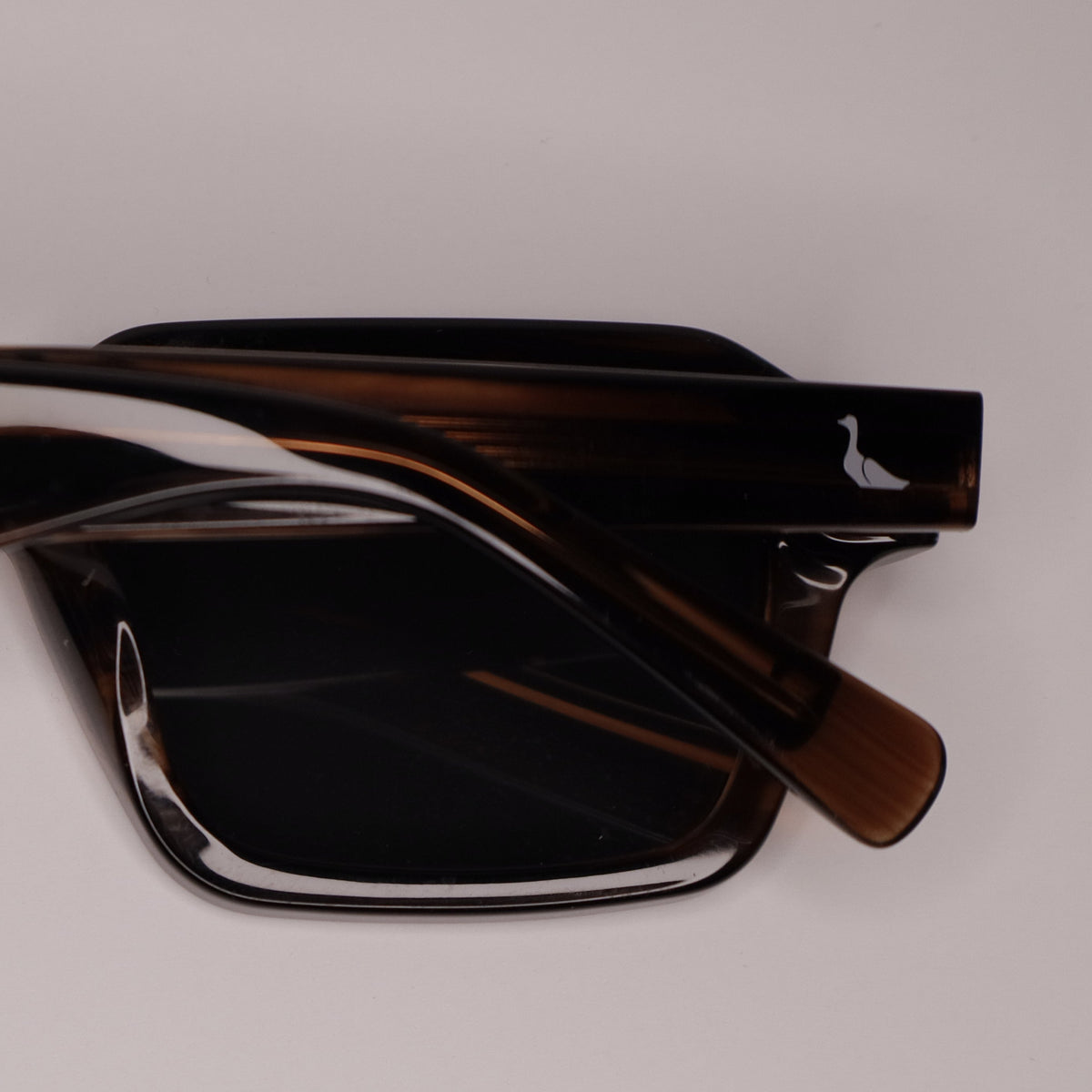 A pair of oversized square sunglasses with a glossy dark brown acetate frame and black lenses, shown from a top-down perspective on a neutral light gray background.